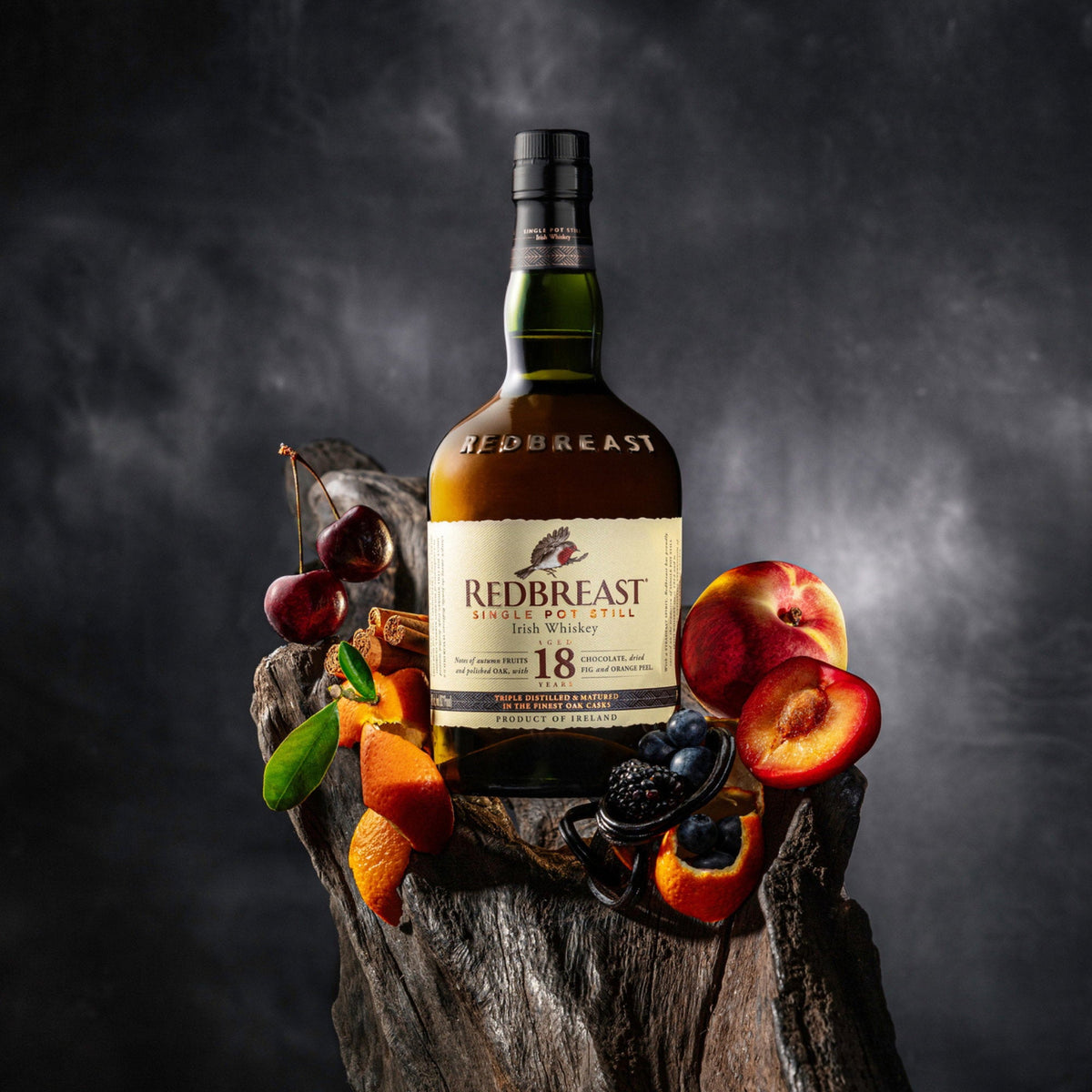 Schwarzbach Spirits Redbreast 18 Year Old Irish Whiskey bottle surrounded by fresh cherries, peaches, and berries.