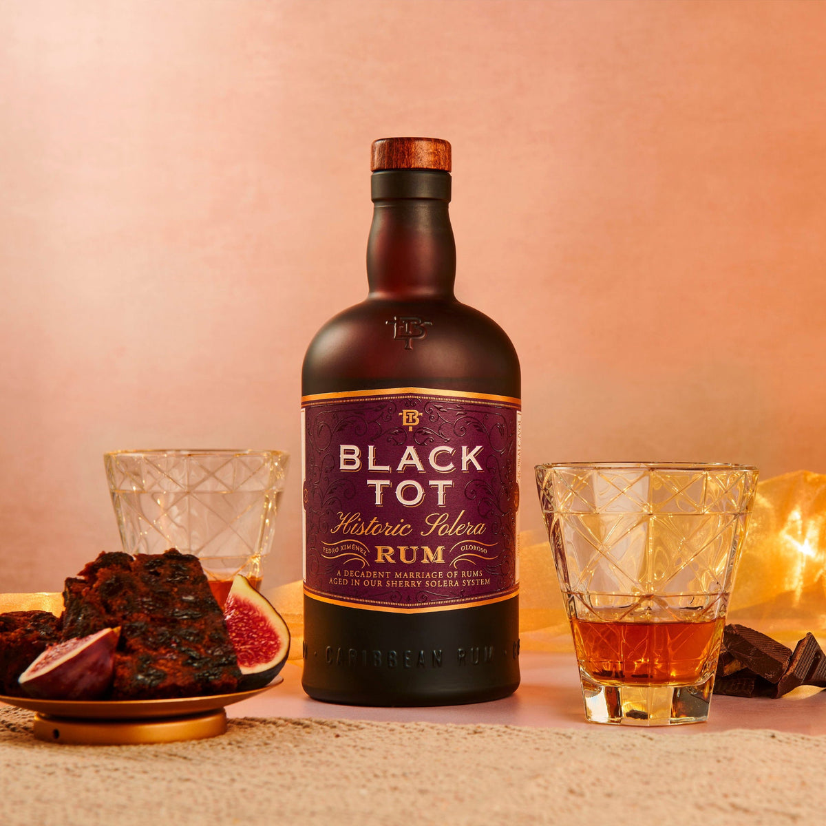 Schwarzbach Spirits Black Tot Historic Solera Rum Flasche mit zwei Gläsern, Feigen und Schokolade auf einem Tisch.