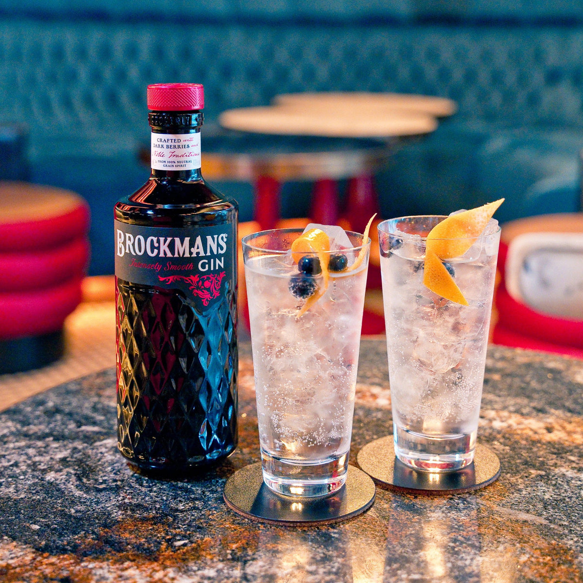 Schwarzbach Spirits Brockmans Gin Flasche neben zwei Longdrink-Gläsern mit Eis, Blaubeeren und Orangenzeste