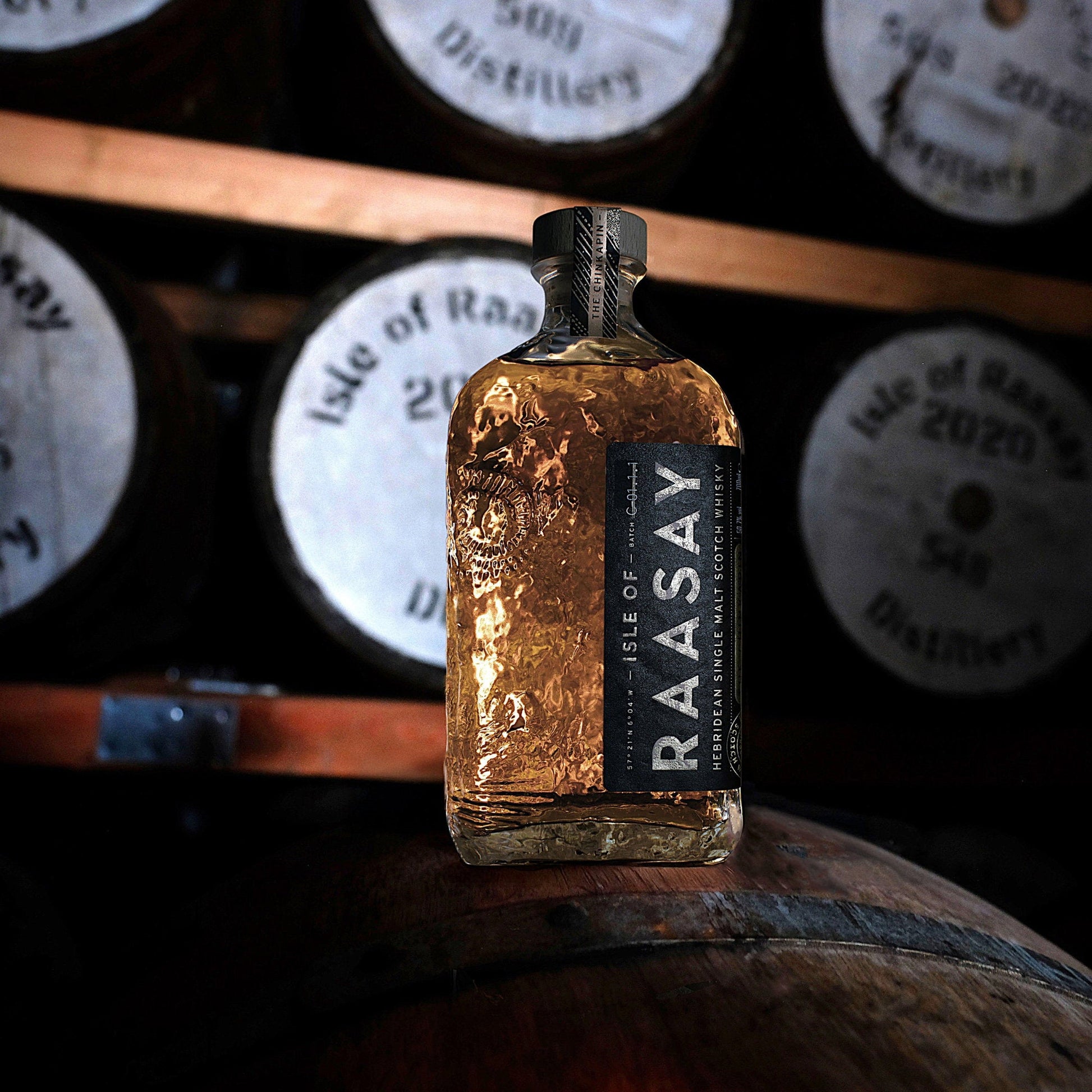 Schwarzbach Spirits Isle of Raasay Chinkapin Oak single malt whisky bottle resting on a wooden barrel in a distillery.