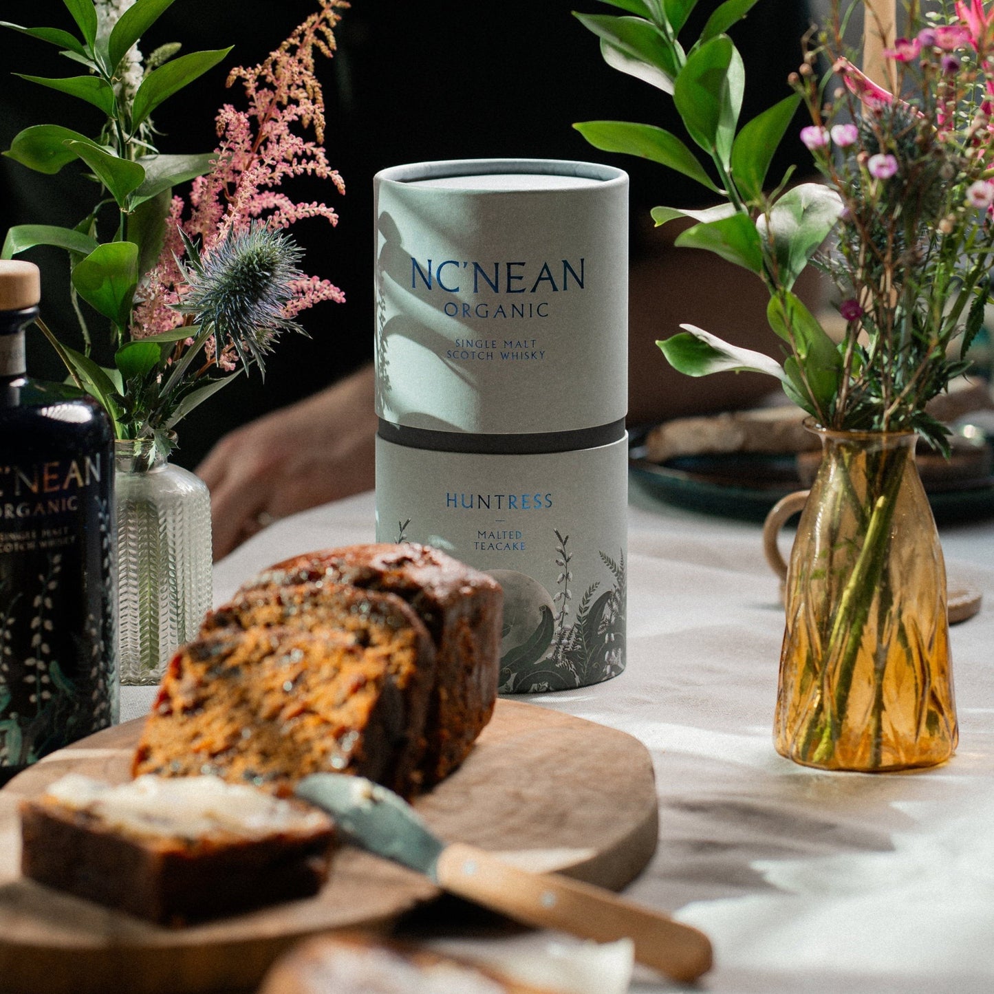 Schwarzbach Spirits: Nc'nean Huntress Malted Teacake Single Malt Scotch Whisky in einer Geschenkverpackung, daneben ein Kuchen.