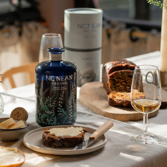 Schwarzbach Spirits NC'NEAN Huntress Malted Teacake Single Malt Scotch Whisky in blauer Flasche neben Kuchen und einem Glas Whisky.