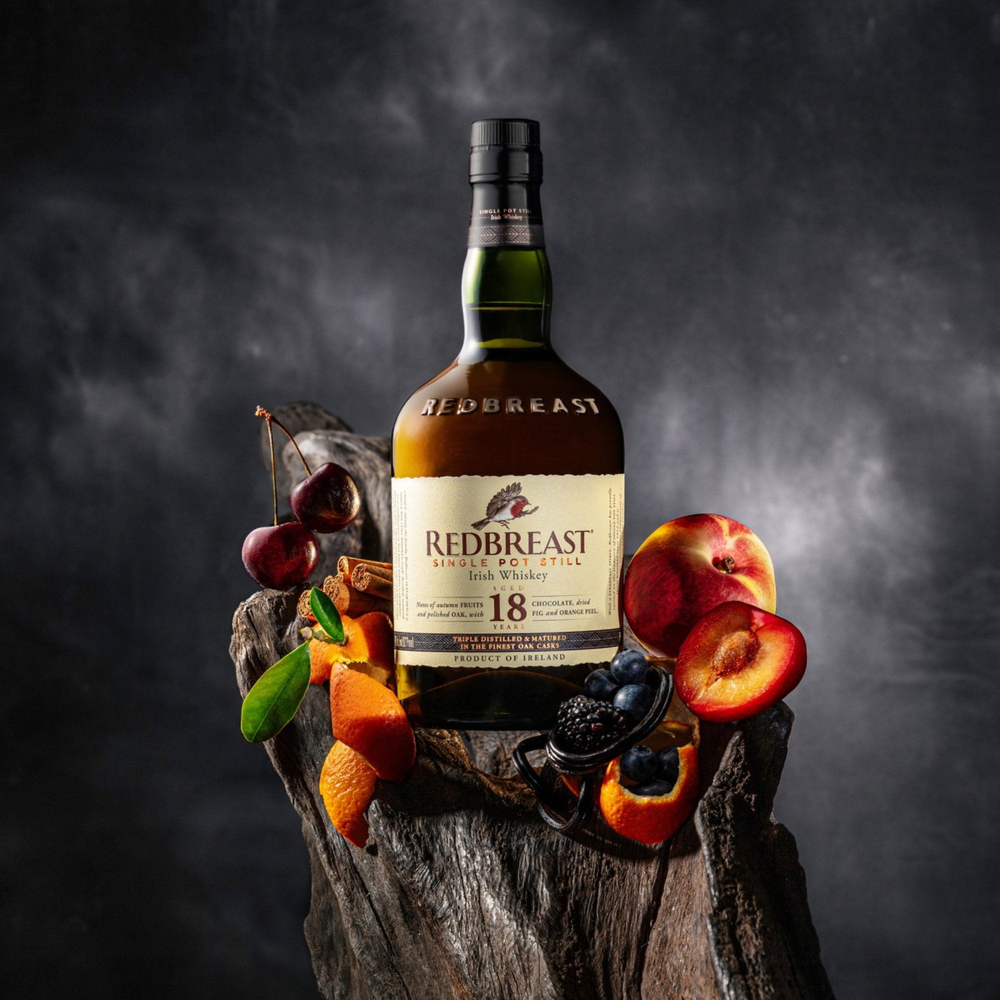 Schwarzbach Spirits Redbreast 18 Year Old Irish Whiskey bottle surrounded by fresh cherries, peaches, and berries.