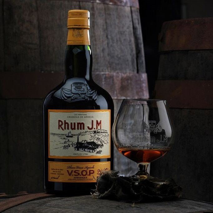 Schwarzbach Spirits Rhum J.M VSOP Agricole Flasche mit gefülltem Schwenker vor einem Holzfass