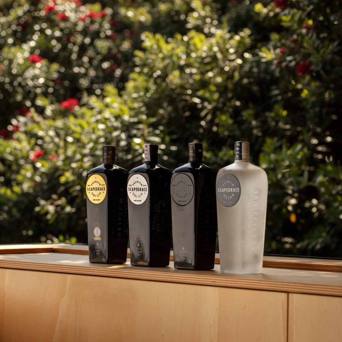 Schwarzbach Spirits Auswahl an Scapegrace Gin und Wodka Flaschen auf einem Holztisch vor einem sonnigen Garten