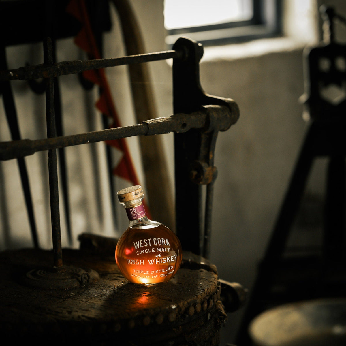 Schwarzbach Spirits West Cork Maritime Port Cask Irish Whiskey in a round bottle on a rustic wooden surface.
