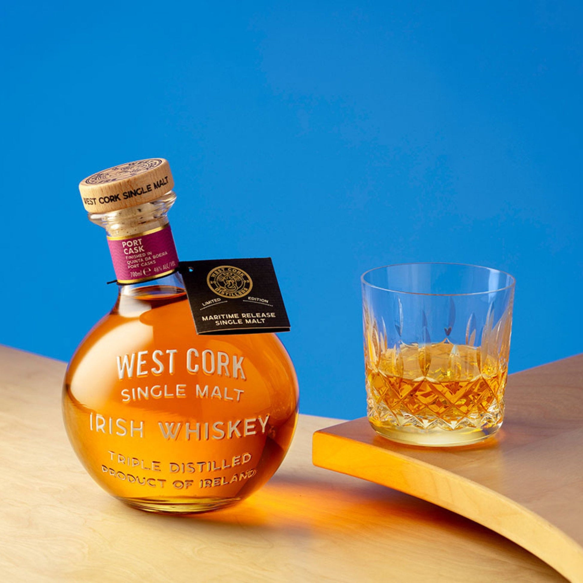 Schwarzbach Spirits West Cork Maritime Port Cask Irish Whiskey in a round bottle next to a glass of whiskey.