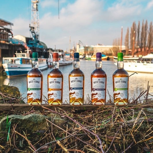Schwarzbach Spirits collection of five West Cork Irish Whiskey bottles with different cask finishes by a harbor.