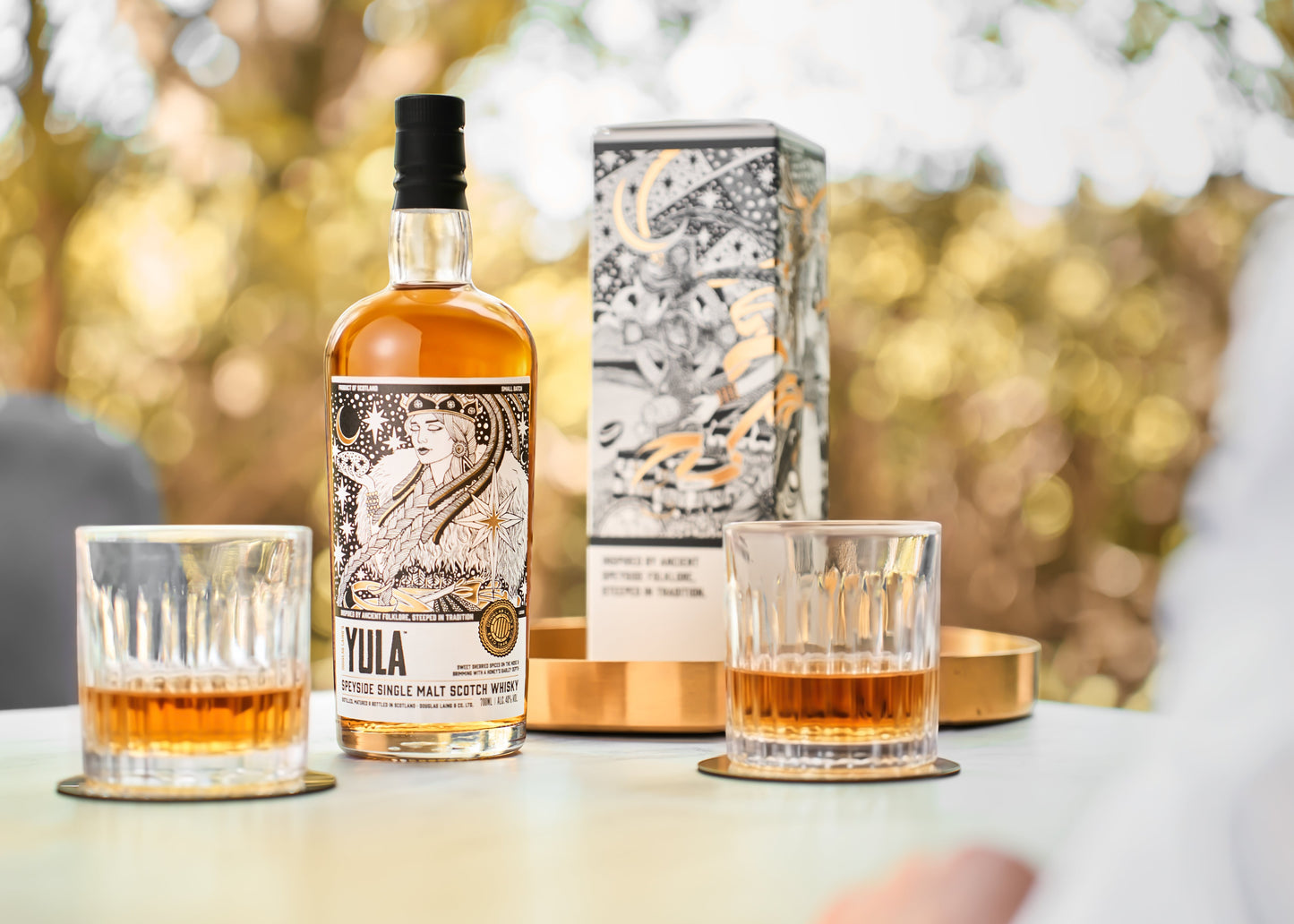 Schwarzbach Spirits YULA Speyside Single Malt Scotch Whisky Flasche mit zwei Gläsern auf einem Tisch im Freien